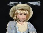 Une poupée en porcelaine vêtue d'une robe et son chapeau...