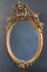 Glace ovale Napoléon III en bois stuqué doré, le fronton...