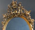 Glace ovale Napoléon III en bois stuqué doré, le fronton...